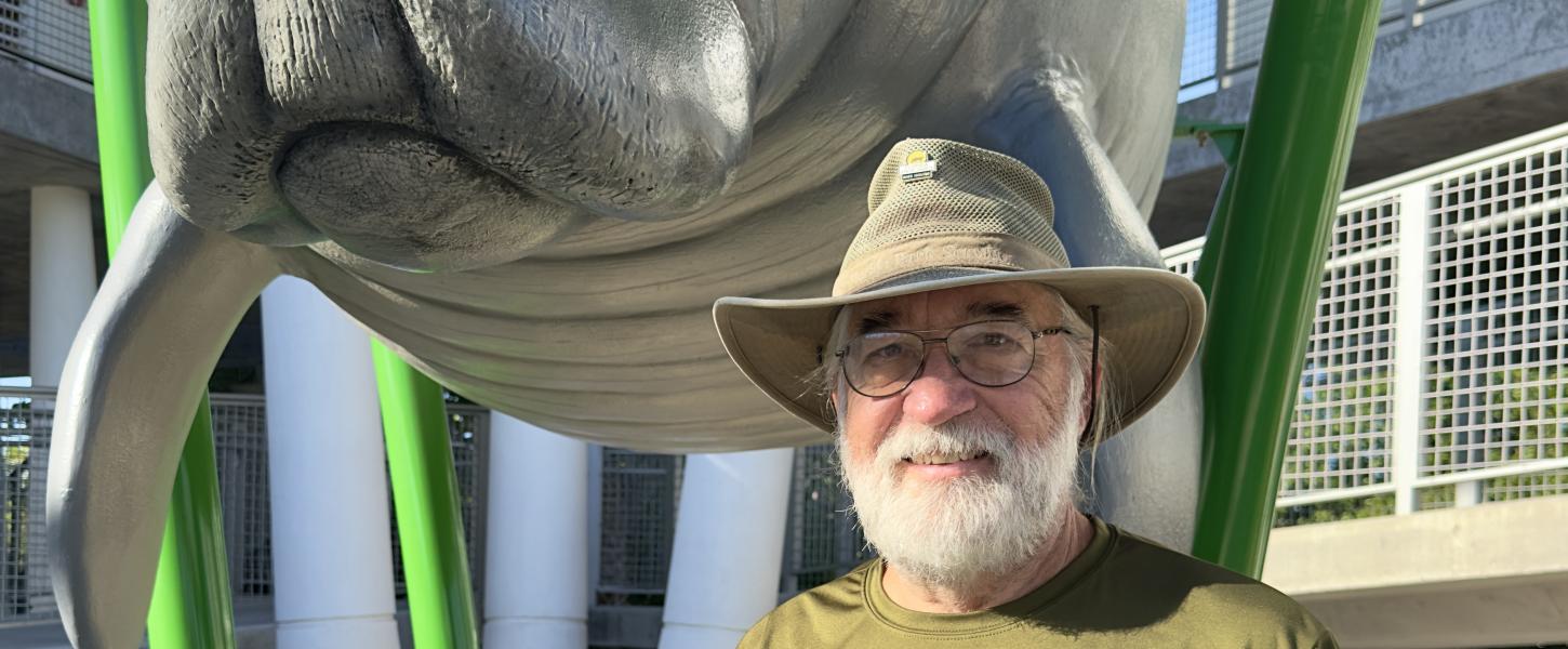 A man in a wide-brim hat standing in front of a manatee statue