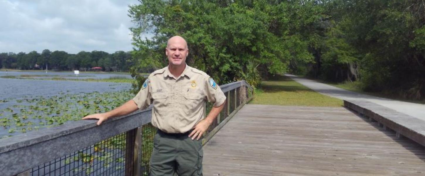 A man in uniform stands on a bridge trail by water