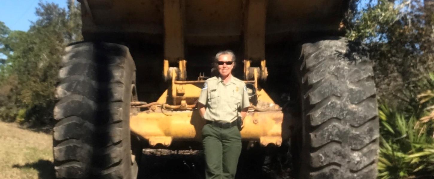 PM Kristin Ebersol standing behind a giant off road dumptruck used for beach clean up