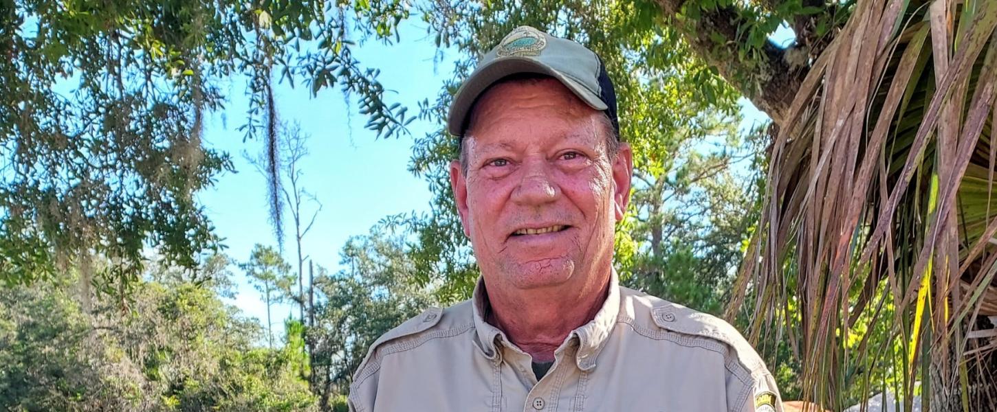 A uniformed park ranger standing outdoors, smiling. 