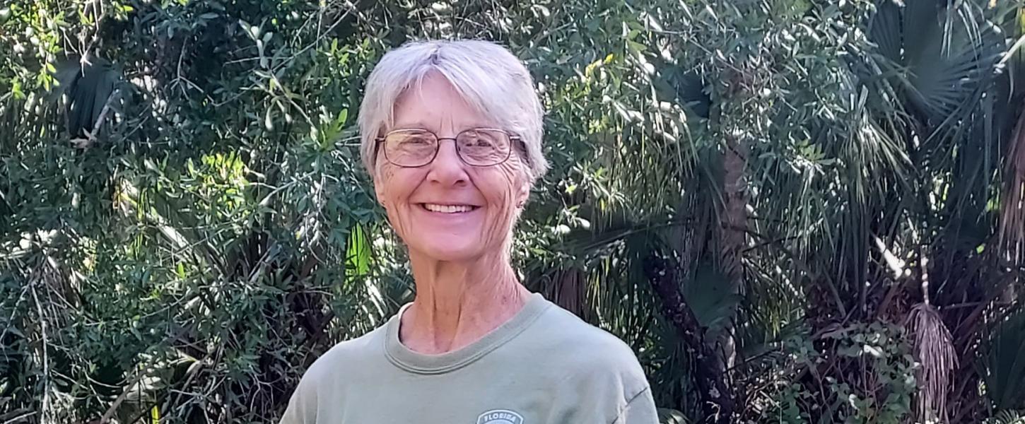 A woman with short hair and glasses standing outdoors, smiling.