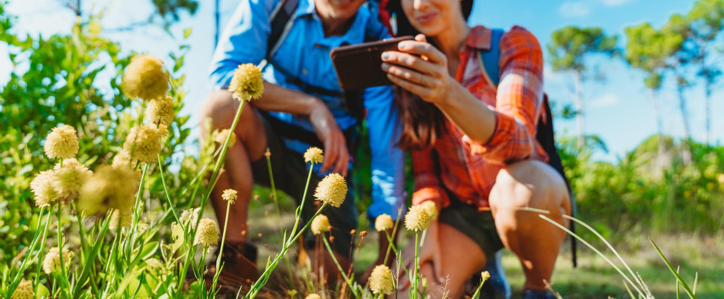 a young couple kneeling with a cellphone to take a picture of a flower 