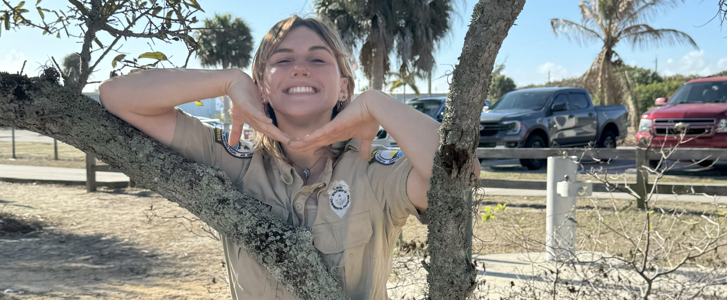 Smiling park ranger leaning on tree. 