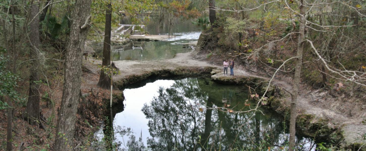 Two peope stand on an outcropping in the spring, next to a unique land bridge.