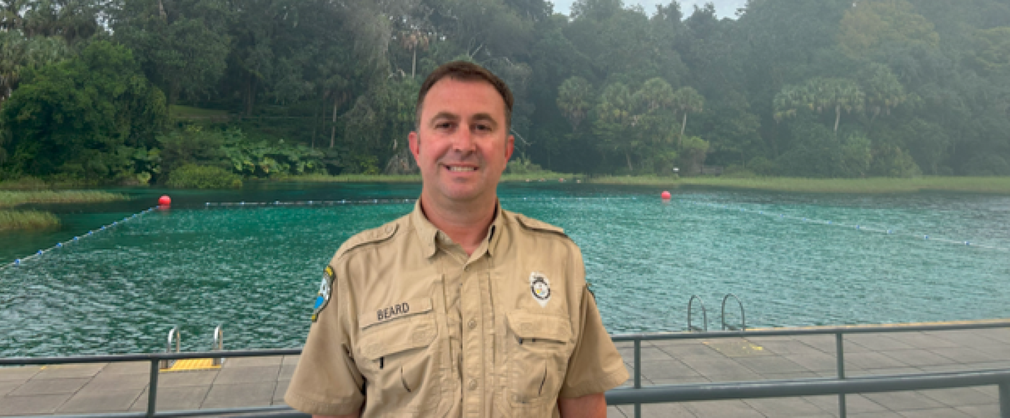 A park ranger standing in front of a swimming area. 