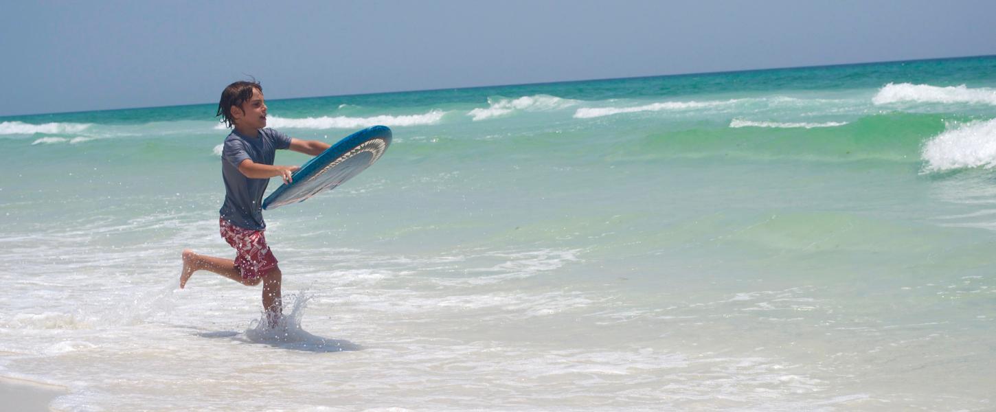 Child on a boogie board running towards the ocean