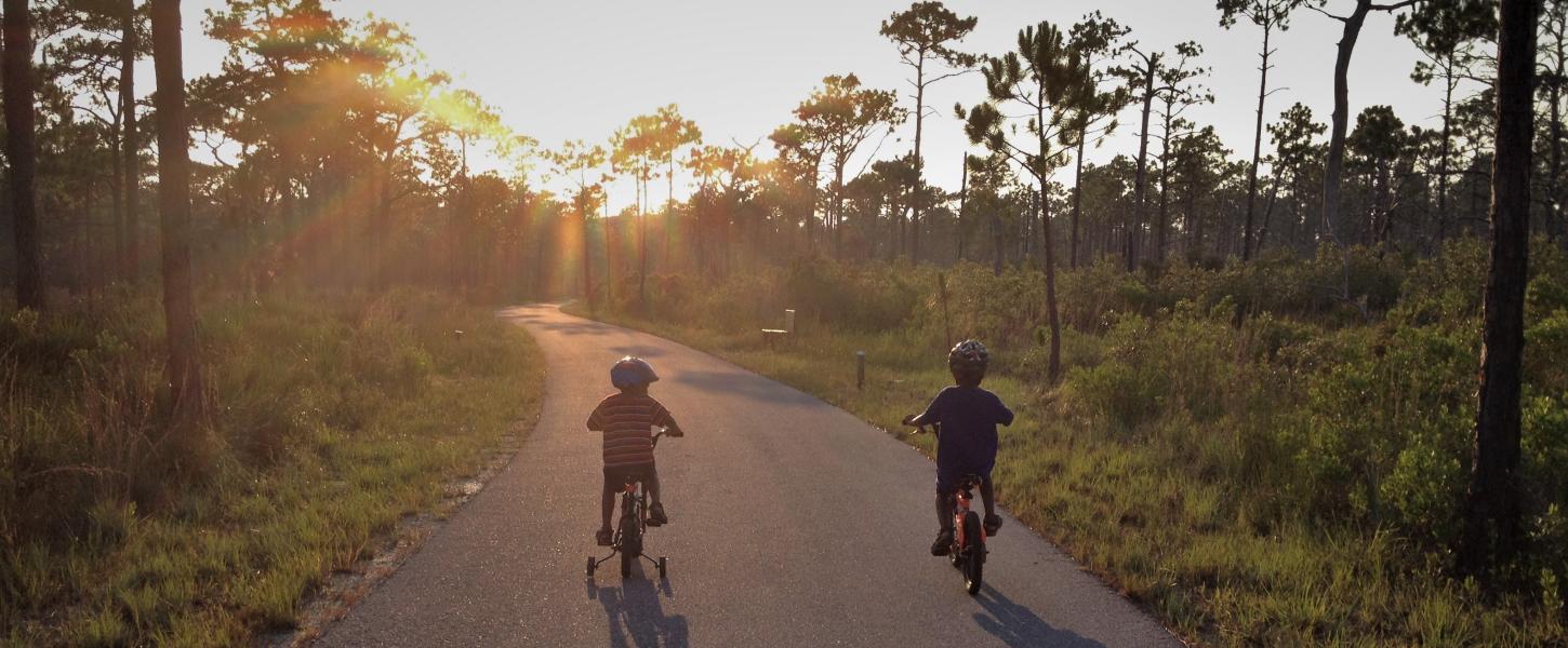 A view of two people walking down the trail with the sun setting in the background.