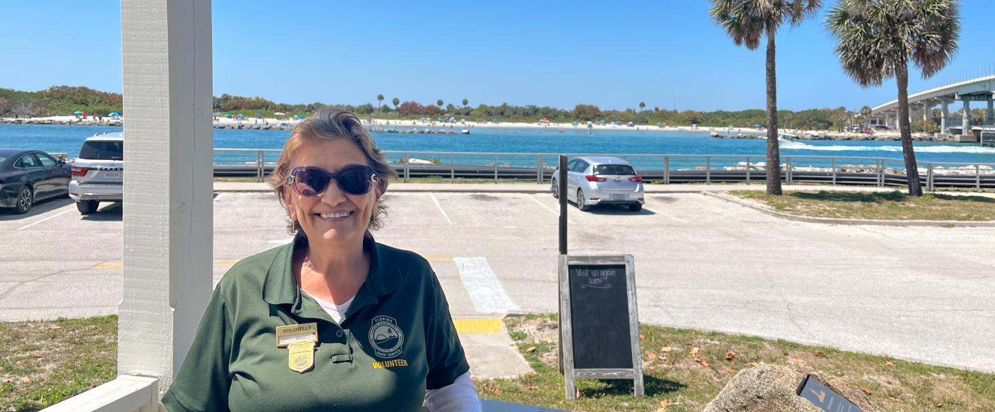 A woman wearing sunglasses, leaning on a railing in front of a parking lot and an inlet. 