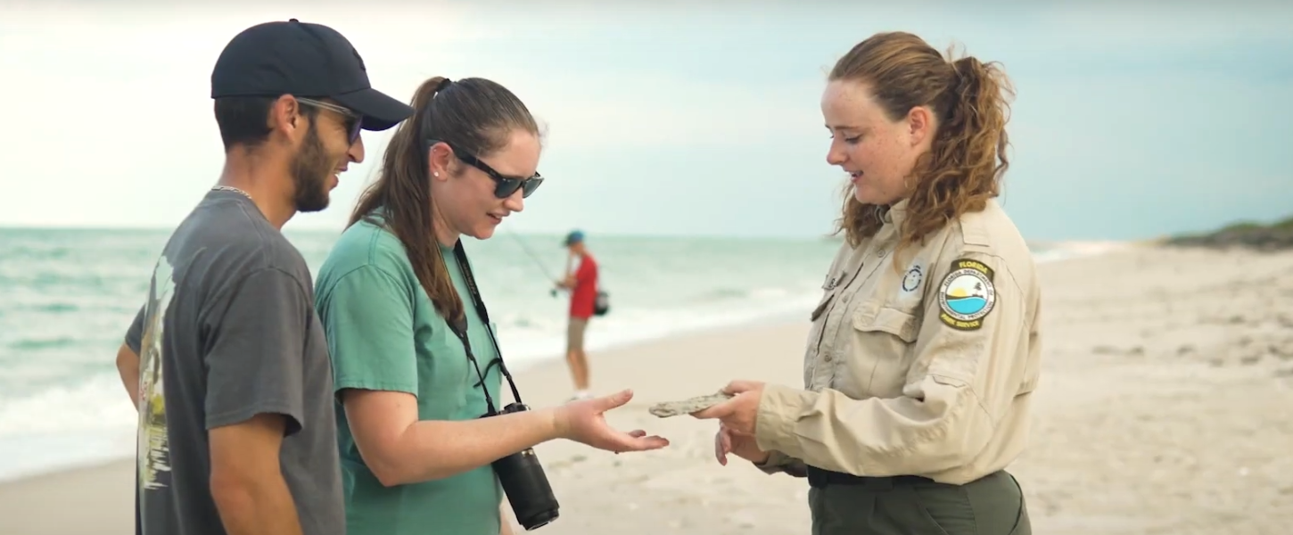 A Park Ranger interpreting to visitors on the beach about a stone that she is holding in her hand. 