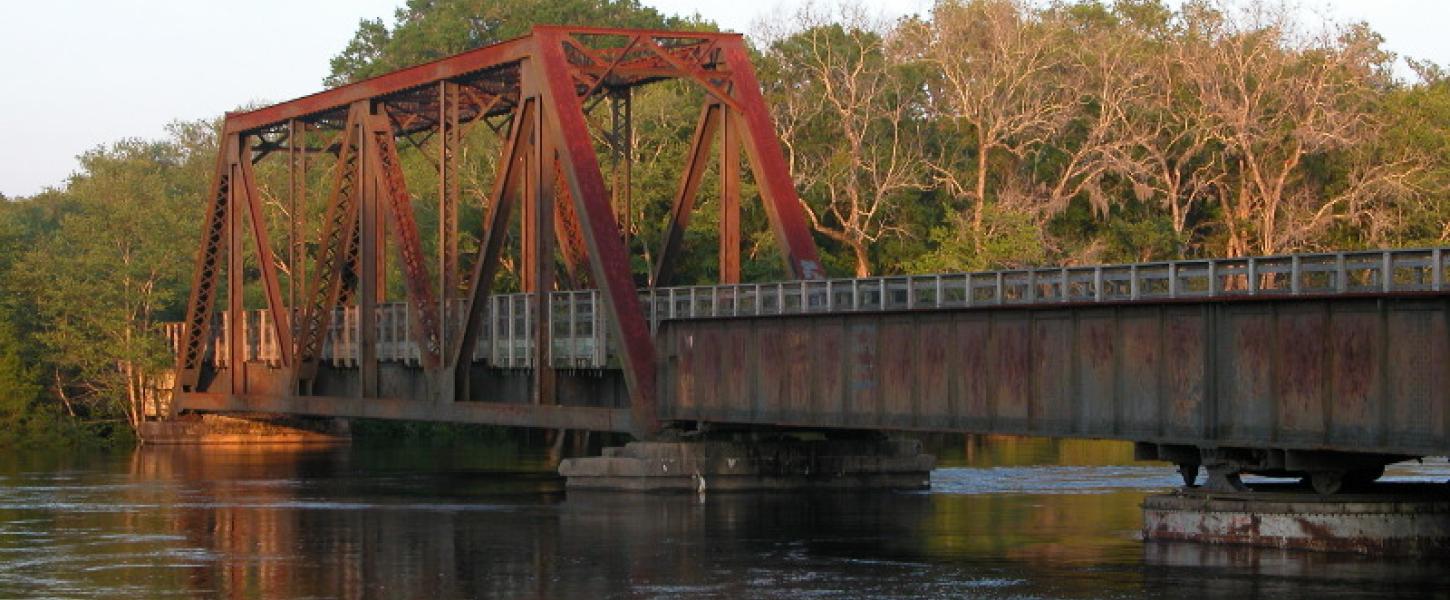 a red steel bridge span extends over a river in the morning light