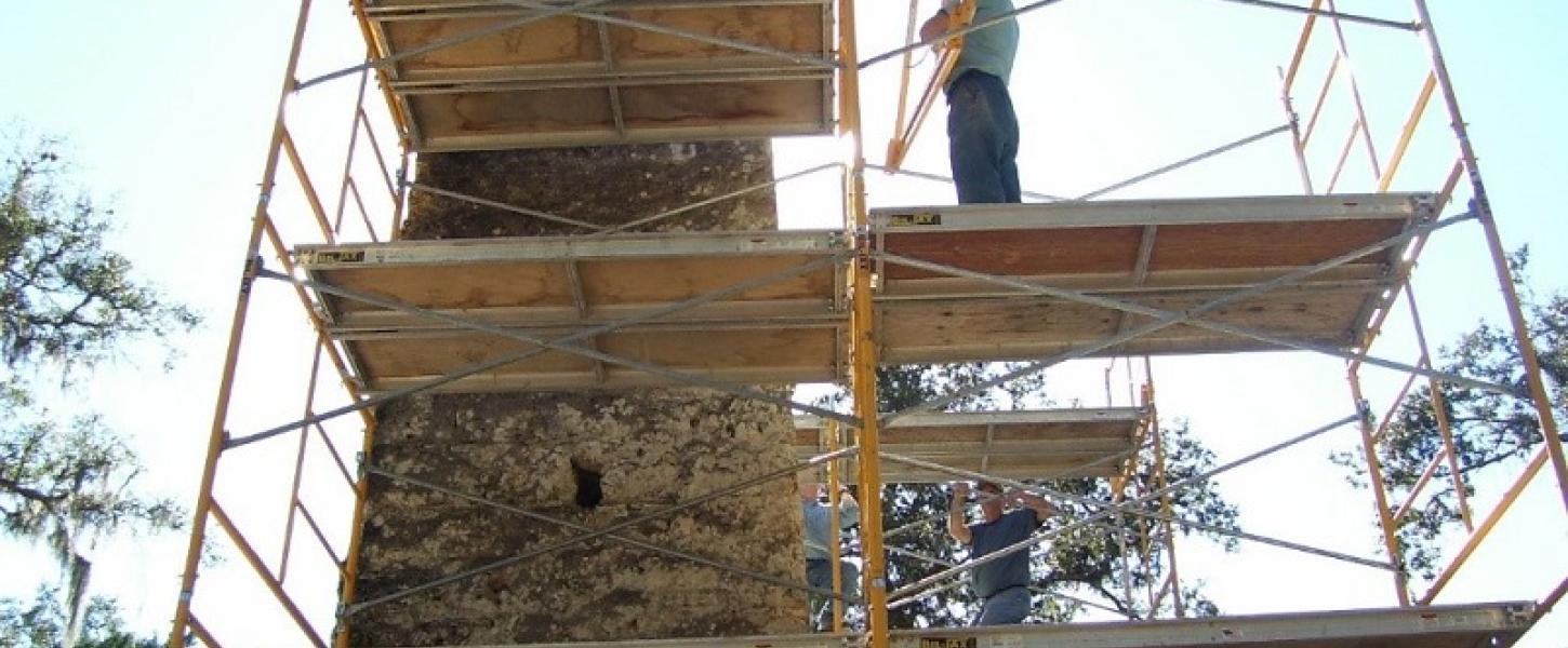 a man stands on several wooden scaffolds surrounding an aged stone chimney