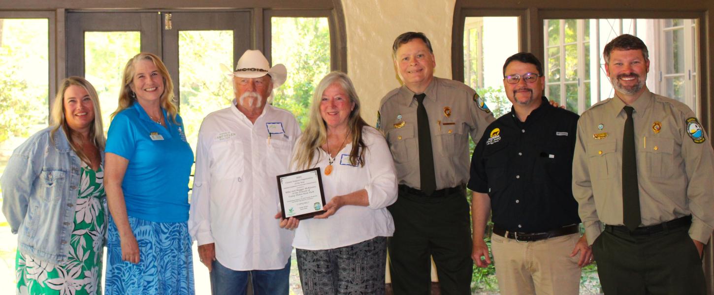 A group of people standing shoulder to shoulder smiling. A man and woman in the center are holding a plaque.