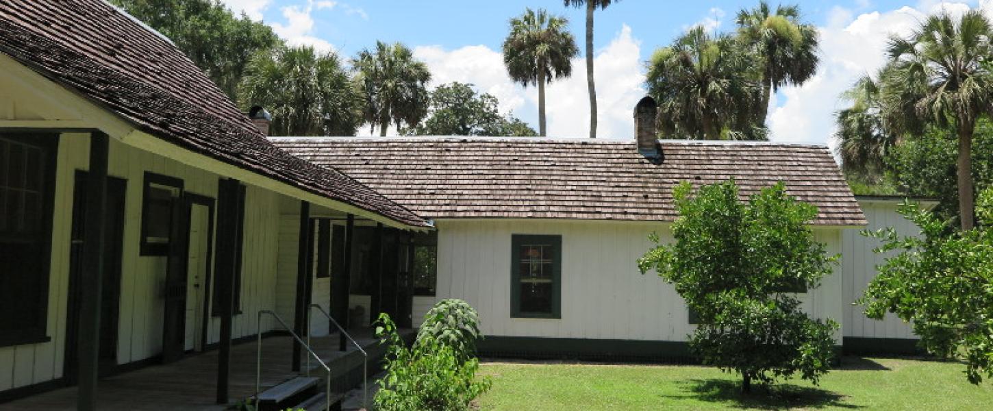 a side view of a yellow and green house surrounded by orange and palm trees