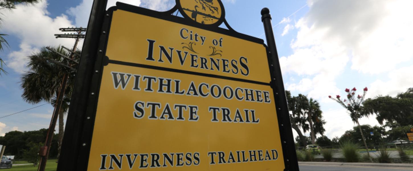 A large yellow and black sign that reads "withlacoochee state trail inverness trailhead"