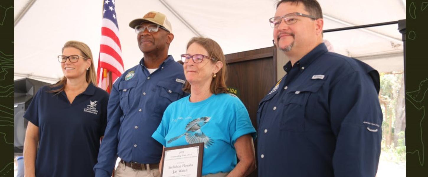 A representative receives the award from Emily Lewis, BJ Givens and Brian Fugate