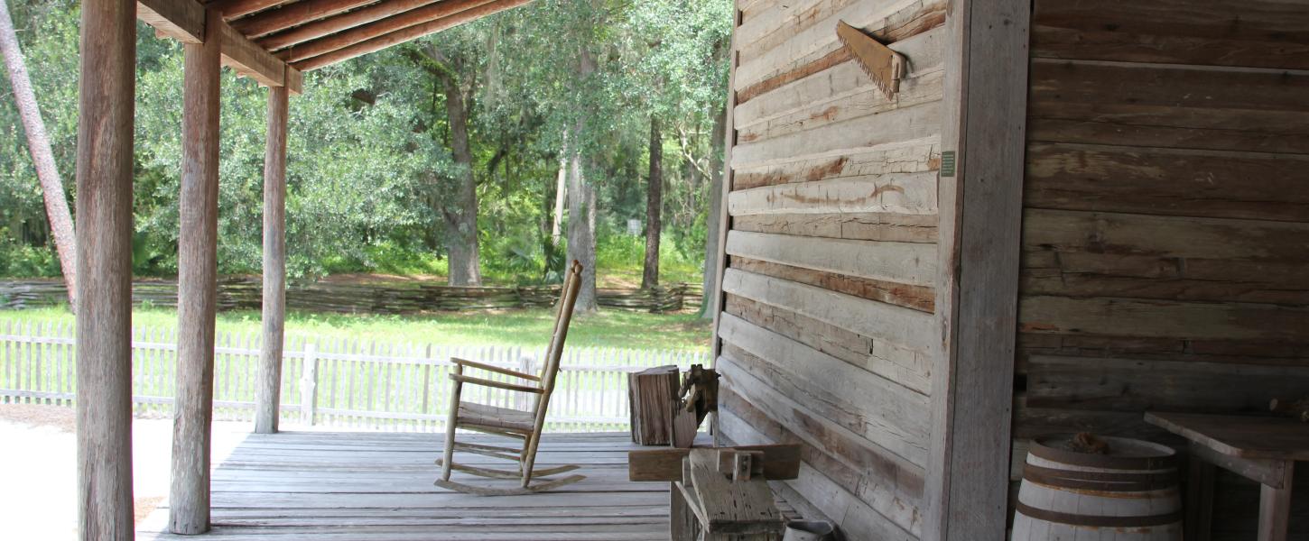 a rocking chairs sits on a wooden porch with antique farming equipment.