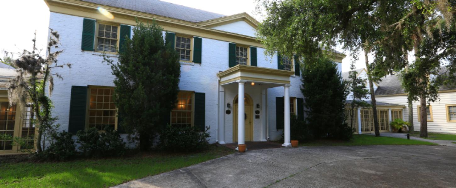 a stately mansion with green and yellow trim next to an oak tree