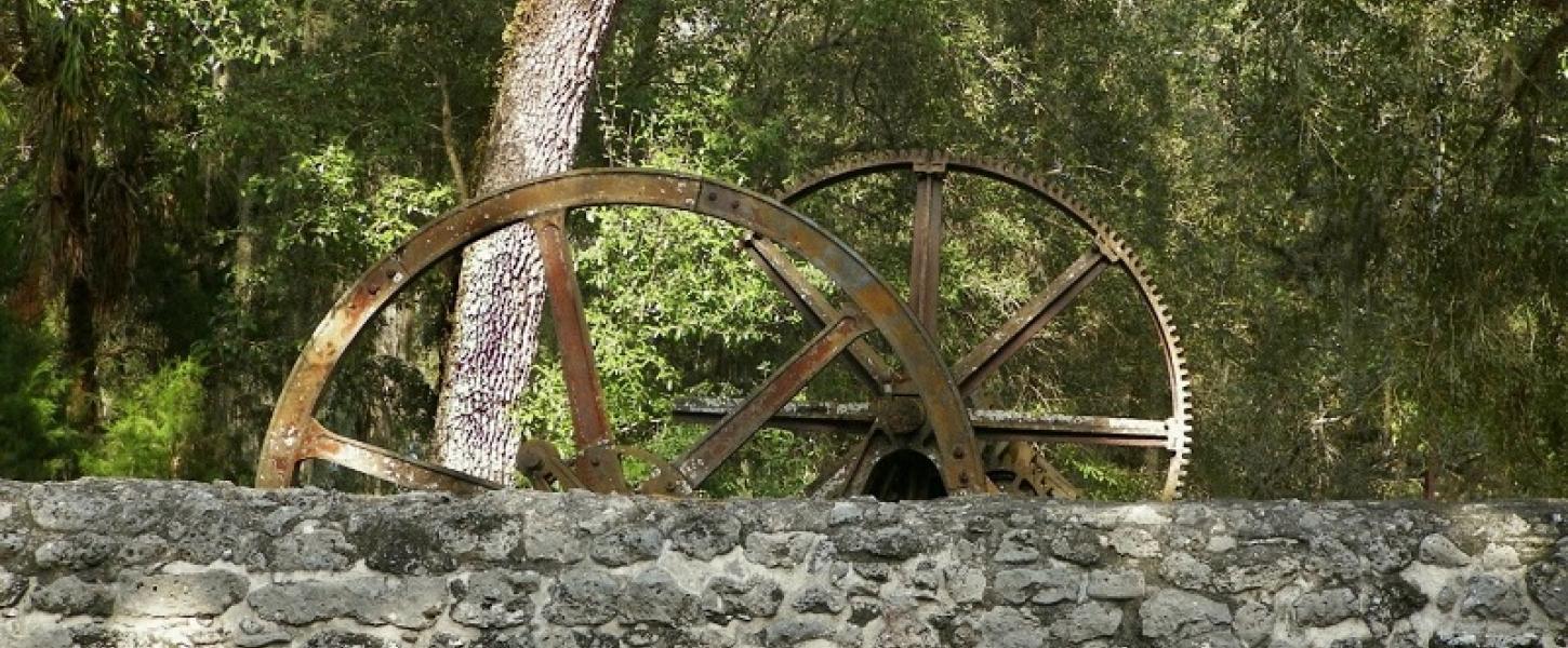 Two large metal rusted wheels above a gray stone wall.