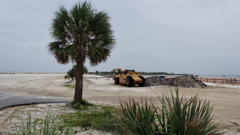 A palm tree stands guard over repairs to the former breach and road.