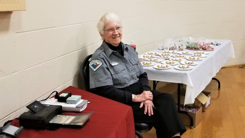 A woman in a grey uniform sits at a table with a red table cloth. 