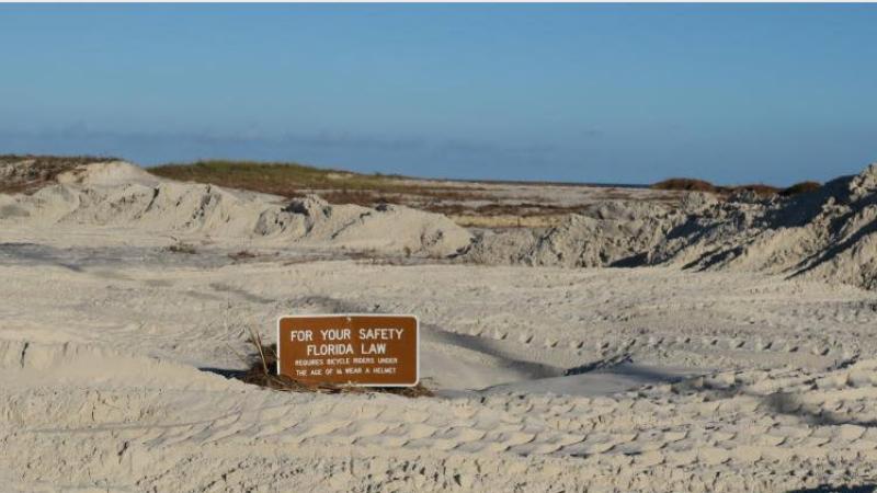 A view of the sand swept on shore by hurricane michael almost covering a sign.