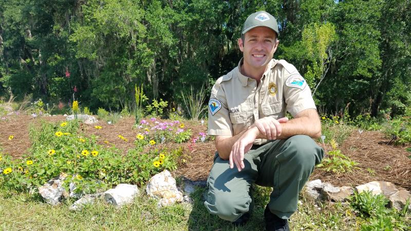 Park Manager of Colt Creek State Park smiling at the camera with a garden behind him