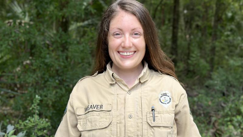 A smiling park ranger standing against a background of forest.