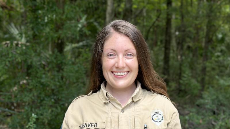 A smiling park ranger standing against a background of forest.