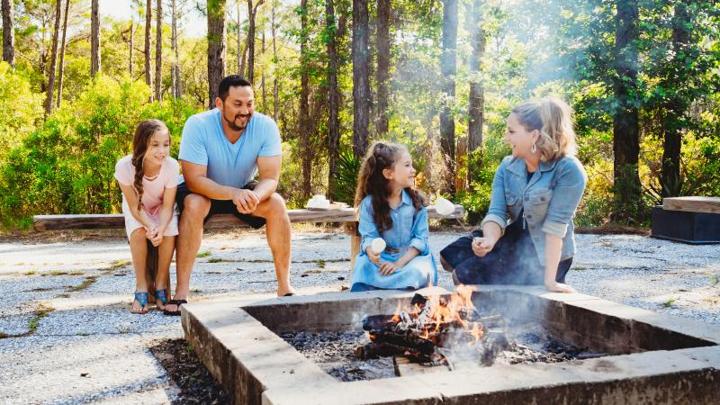 A family of four roasts marshmallows over a fire pit.