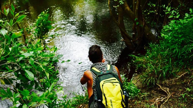 A view of a man sitting by a the river with a yellow backpack.