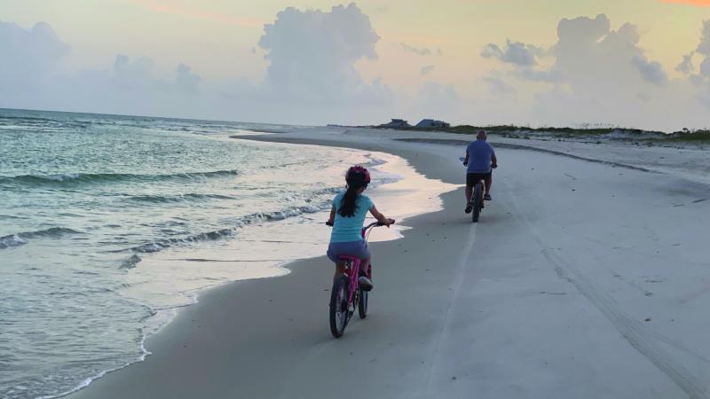 Two people ride bicycles on the beach.