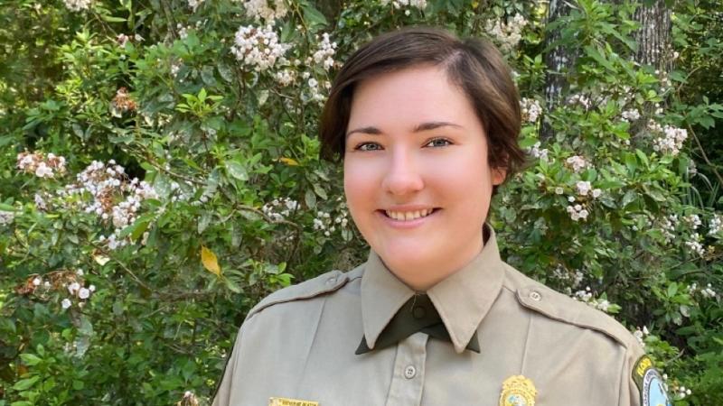 A park ranger in front of a flower bush