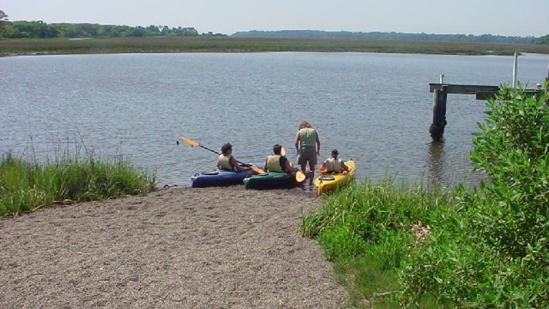 3 kayaks are launched into the water at a sandy ramp.