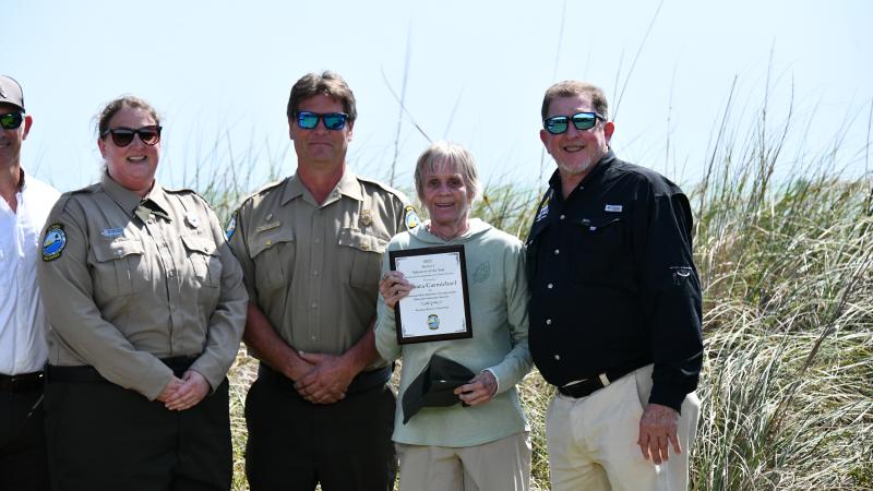 volunteer smiling holding award plaque surrounded by park staff