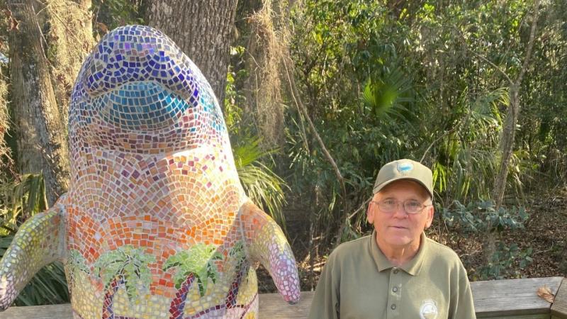 Volunteer Ronnie Coffman poses beside a dolphin statue.