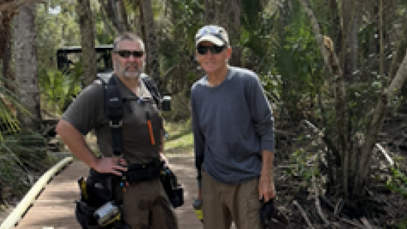 Two men with an assortment of tools standing on a newly-built elevated boardwalk. 