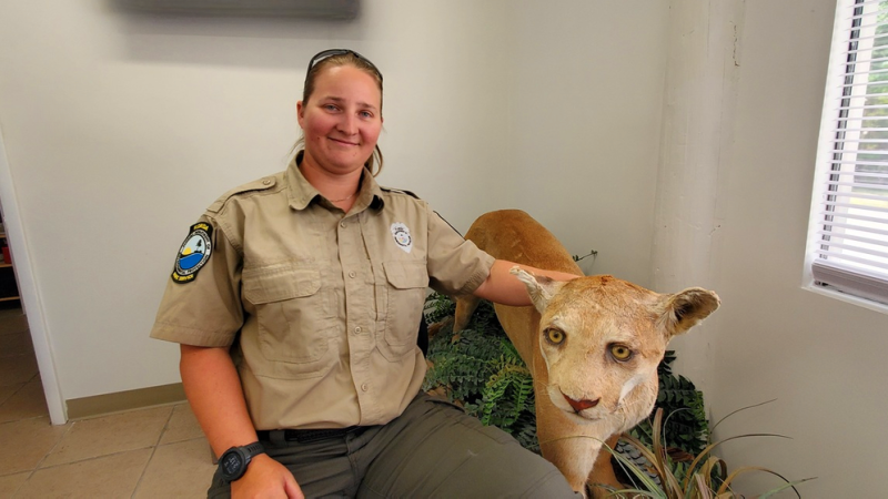 Person seated wearing tan shirt and green pants. Florida panther