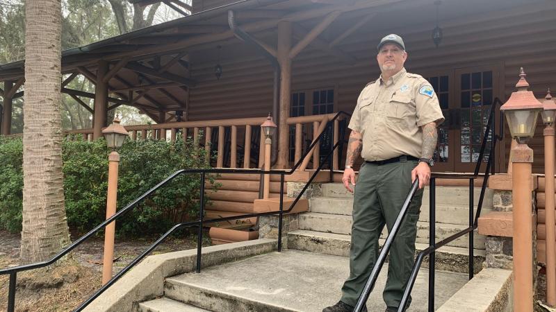 Park Ranger Clayton Iron Wolf stand on the steps leading up to the Lodge at Camp Helen State Park. 
