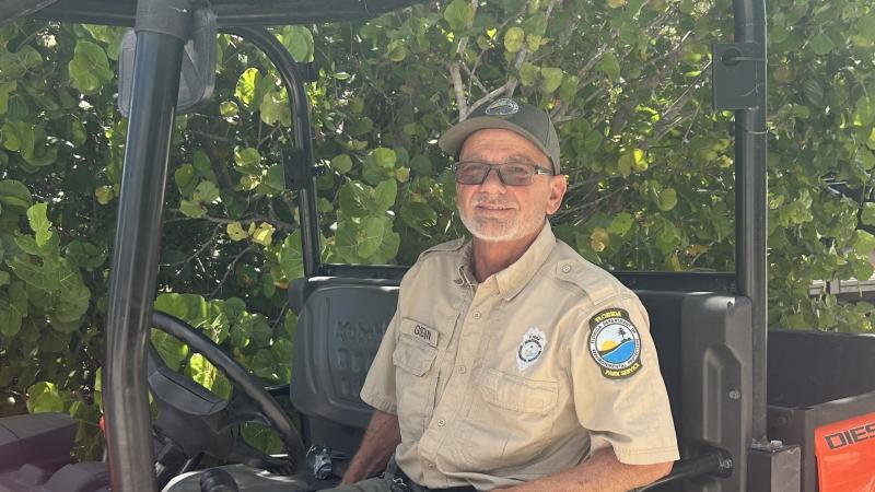A park ranger in the drivers seat of a UTV, with a background of sea grape plants. 