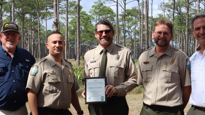 a group of park service staff standing shoulder to shoulder. The park ranger in the middle is holding a plaque. 