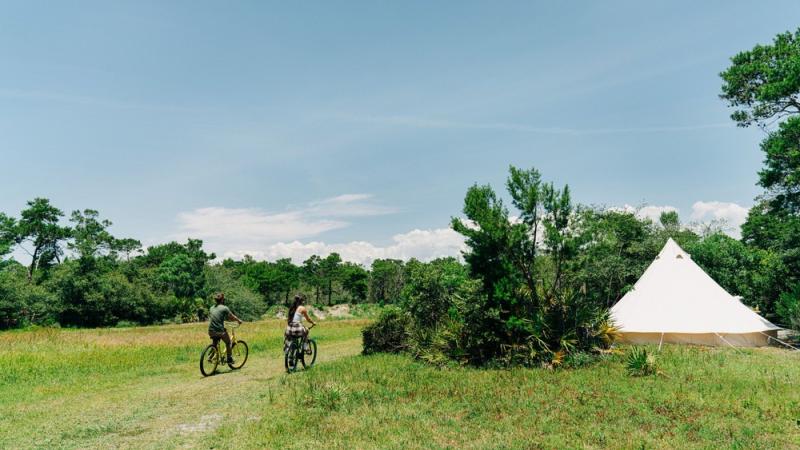 Two people ride bikes towards Fancy Camps tent.