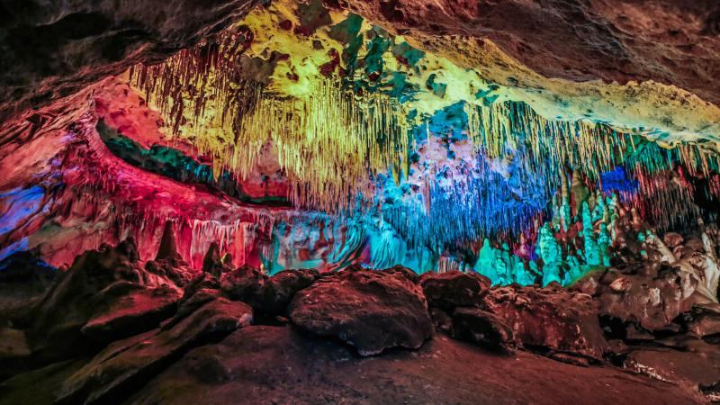 Cave formations on floor and ceiling illuminated by colored lights. 