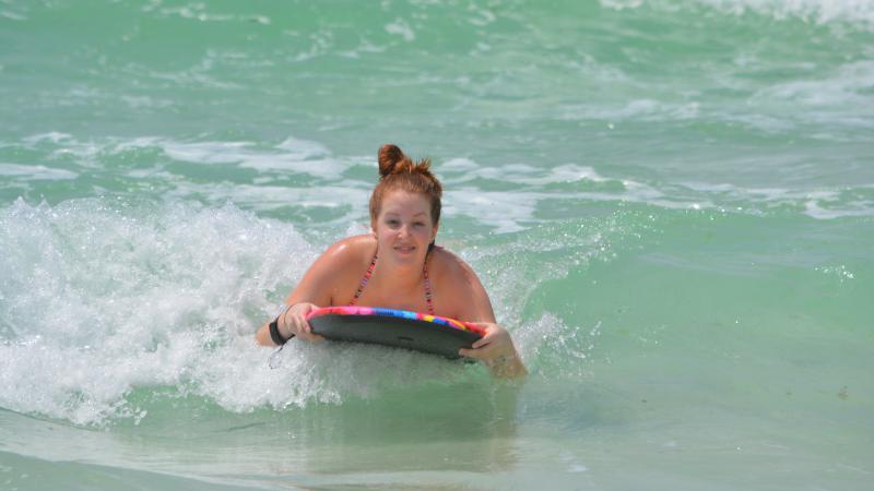 Young girl is all smiles as she glides on wave on her surfboard in emerald green waters. 