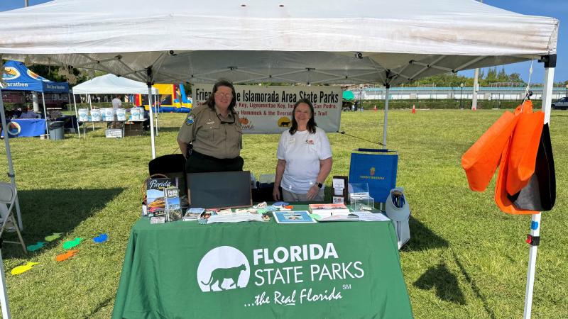 Two women at a themed table outside under a pop-up pavilion. 