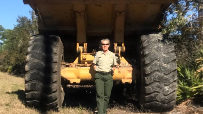 PM Kristin Ebersol standing behind a giant off road dumptruck used for beach clean up