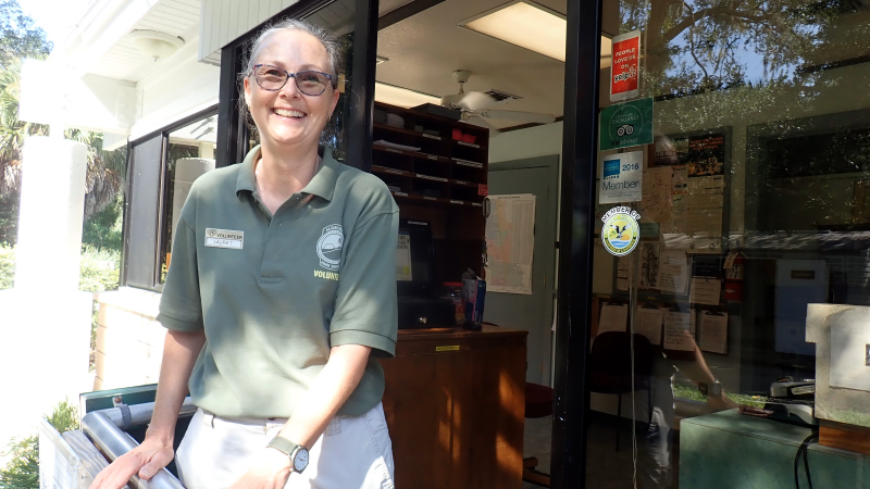 A smiling woman in a volunteer polo at a ranger station. 