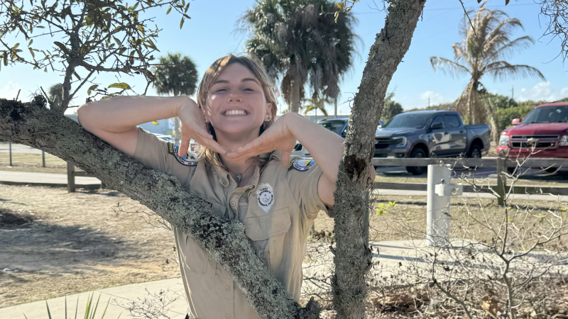 Smiling park ranger leaning on tree. 
