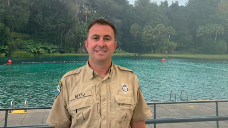 A park ranger standing in front of a swimming area. 