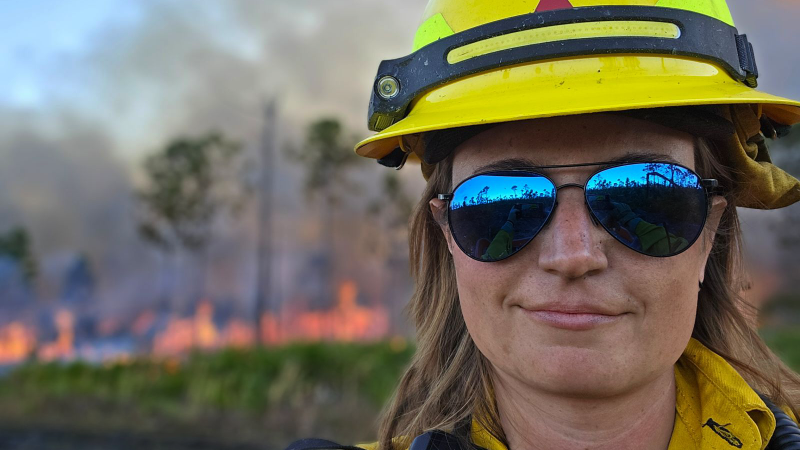 A woman wearing protective fire safety equipment and reflective aviator sunglasses.