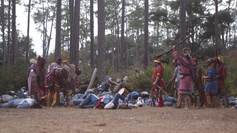 Seminole reenactors in colorful garb raise their rifles in celebration after their victory of the soldiers.